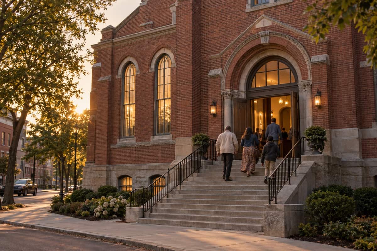 Families climbing the front steps of a historic brick building at golden hour